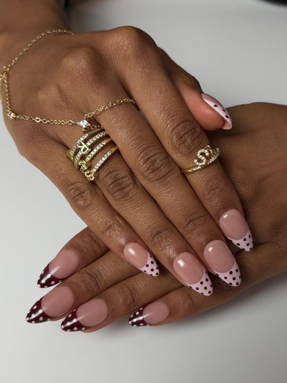 Hand with gold rings and polka dot nail design on a white background